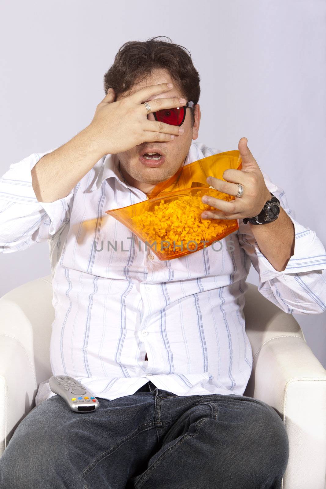 A young man watching a movie in 3D, with stylish 3D glasses and eating popcorn.