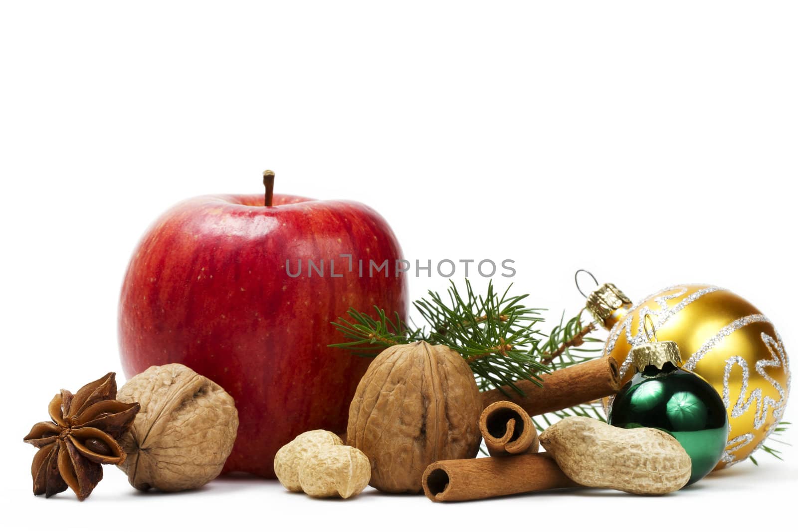 red apple, star anise, some nuts, golden and green christmas balls and a branch on white background