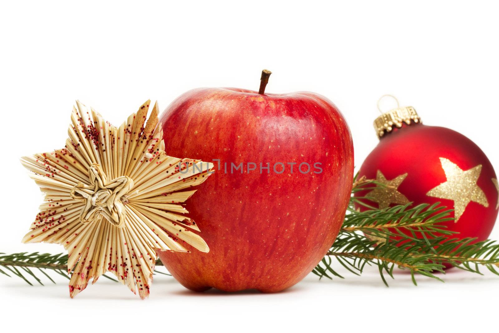 red apple, a straw star and a red christmas bauble in background with a branch on white background