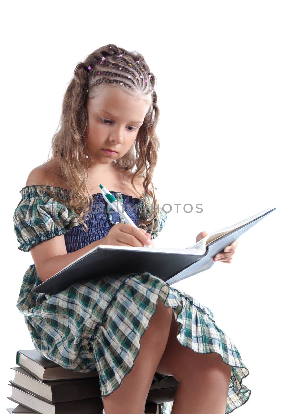 Little girl sitting on stacked books and writing in notebook, isolated on white background 