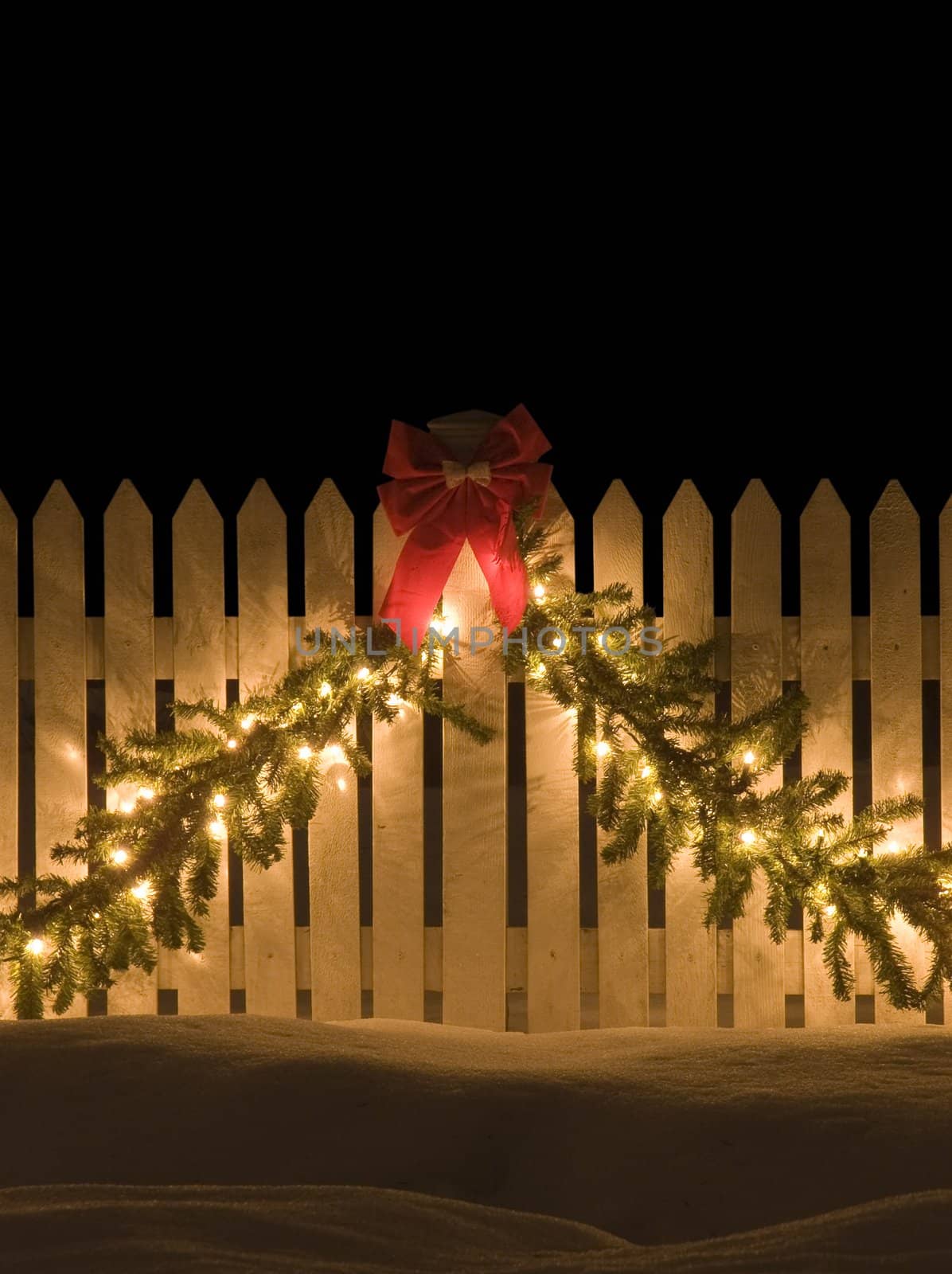 White picket fence decorated for christmas with lights and bow