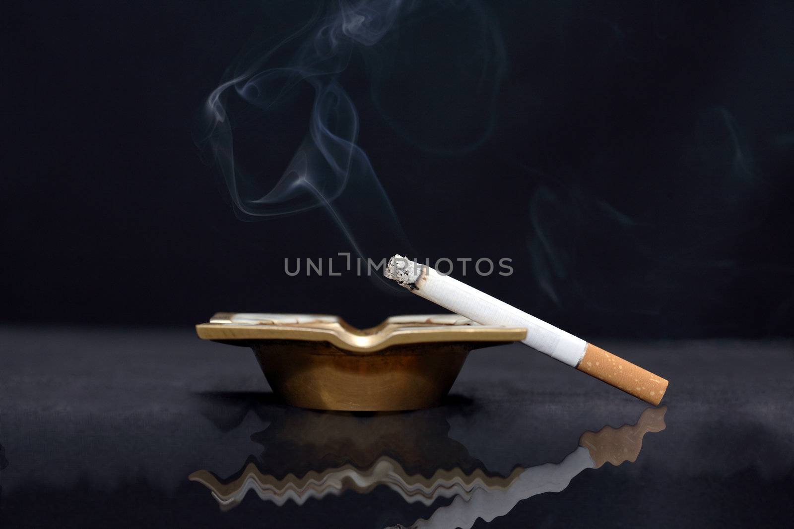 Closeup of smoking cigarette lying on old bronze ash-tray on dark background