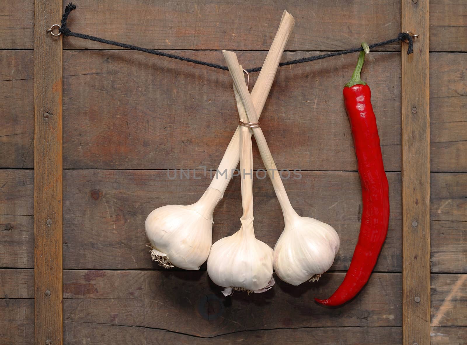 Garlic and chili pepper hanging with rope on wooden background