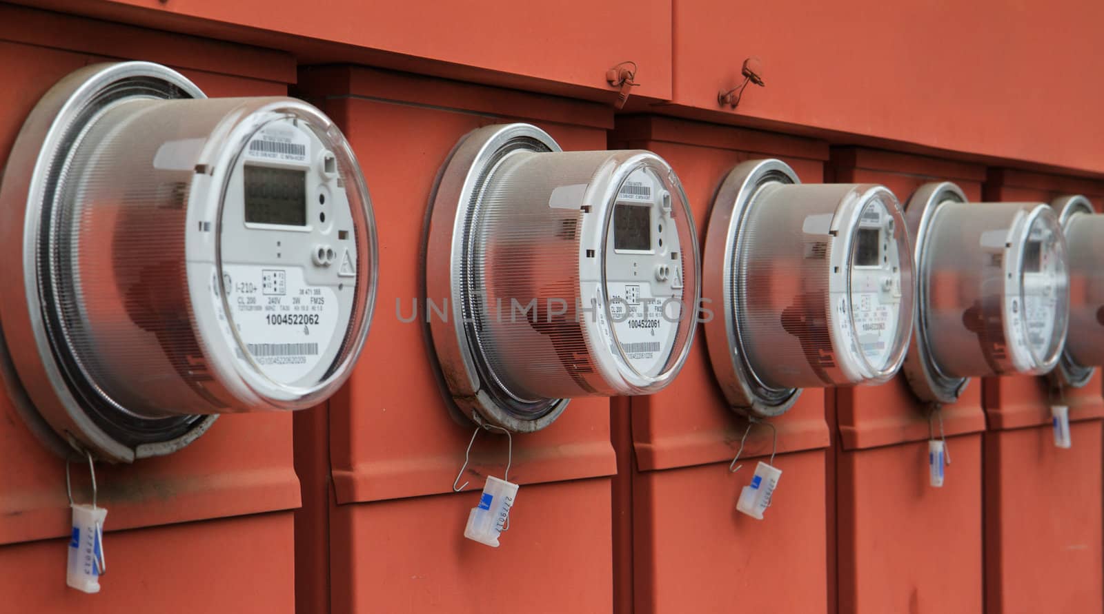 Line up of five elecric power meters on red electrical panels