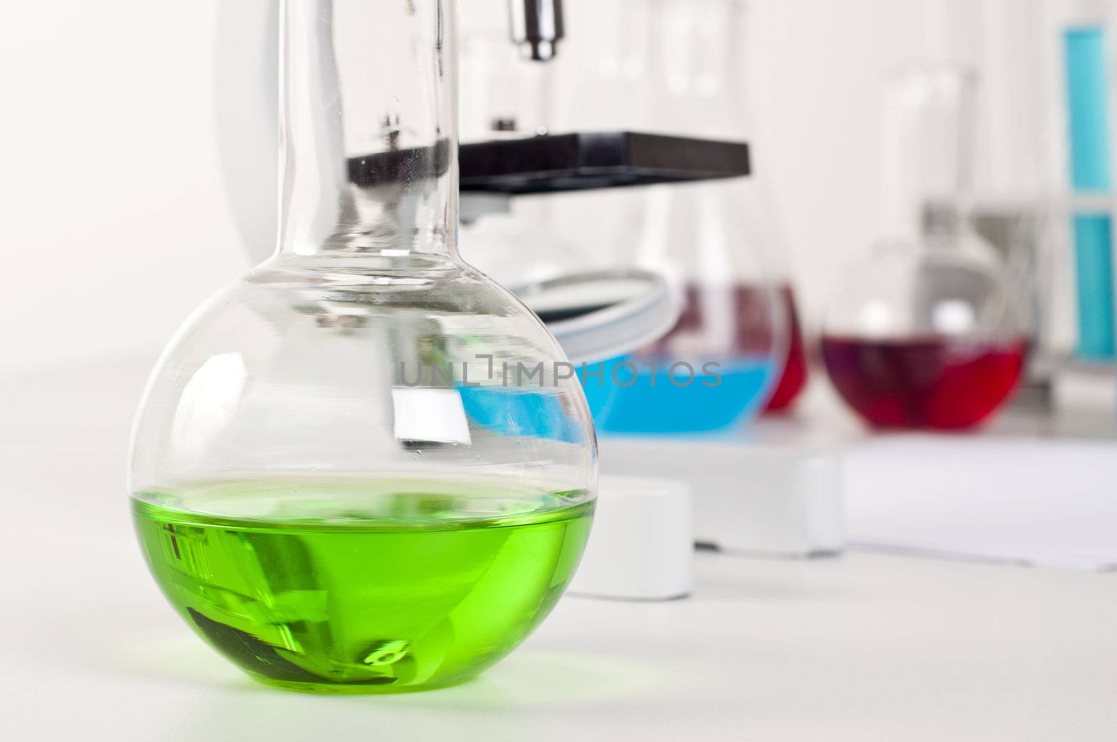 lab bottle with green liquid, in the background microscope and other items