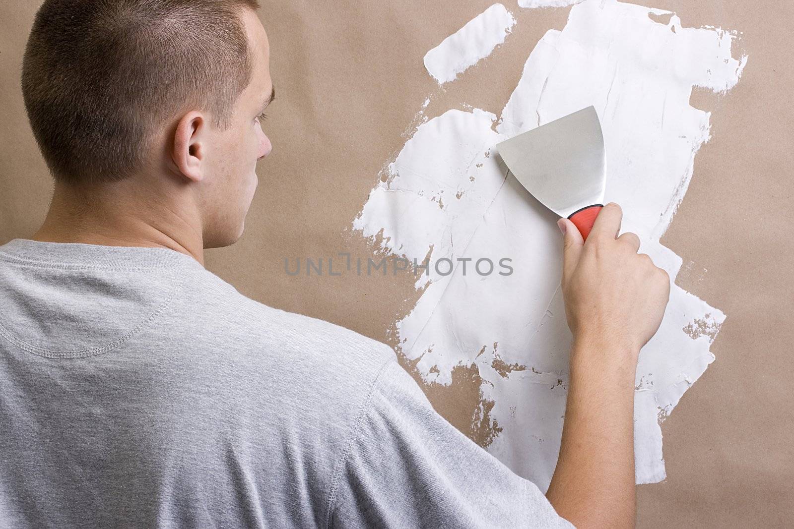 Caucasian man plastering a brown wall with a pallet.