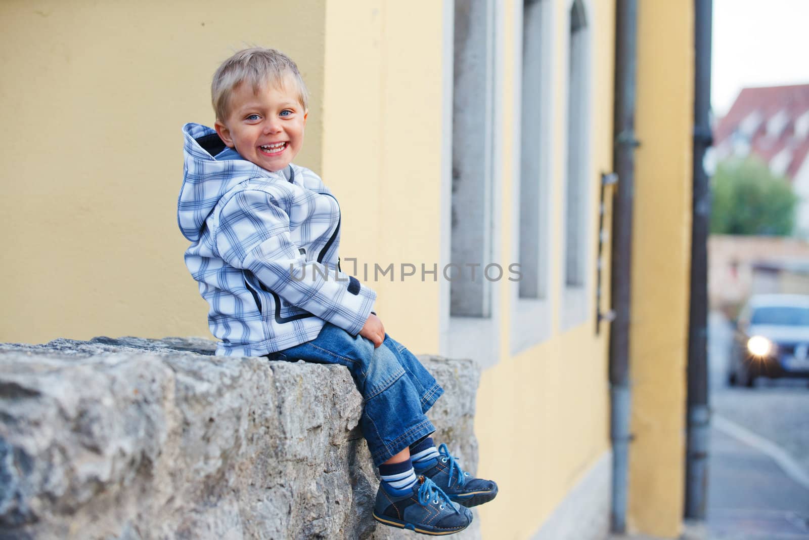 Cute little boy sits near the old house on a city street. Germany