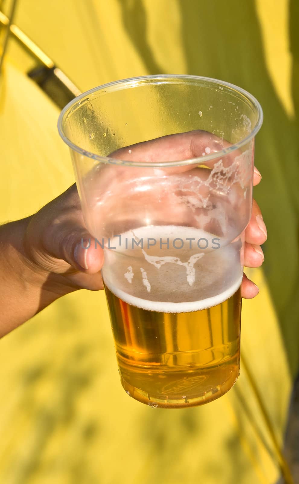 Woman's hand with a glass of beer on a yellow background. Outdoor, summer.