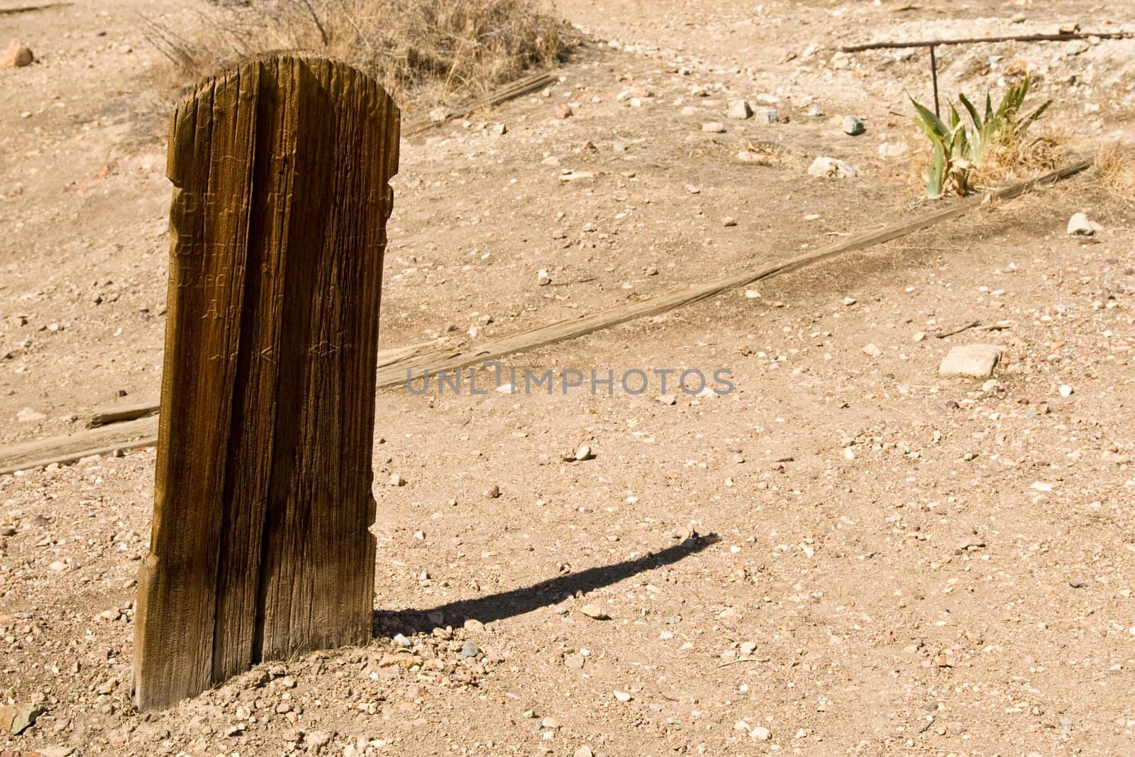 Desert graveyard scene of very worn wooden plank casting a long shadow on dirt
