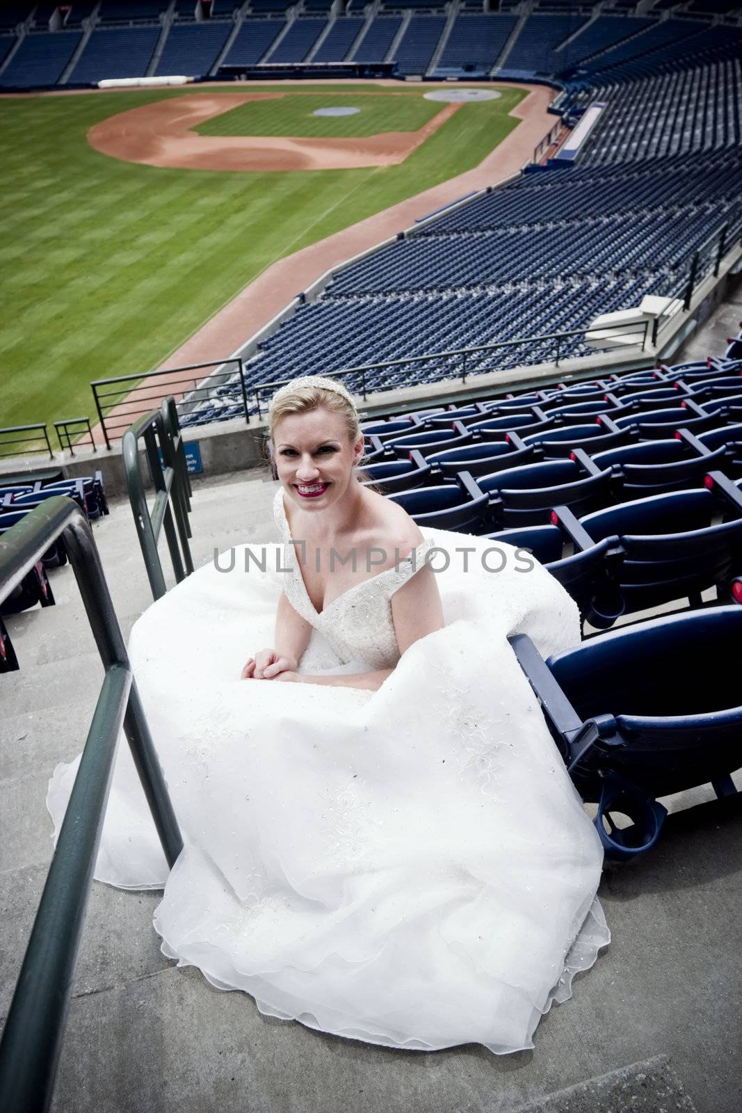 Model wearing wedding gown posed in a baseball stadium.