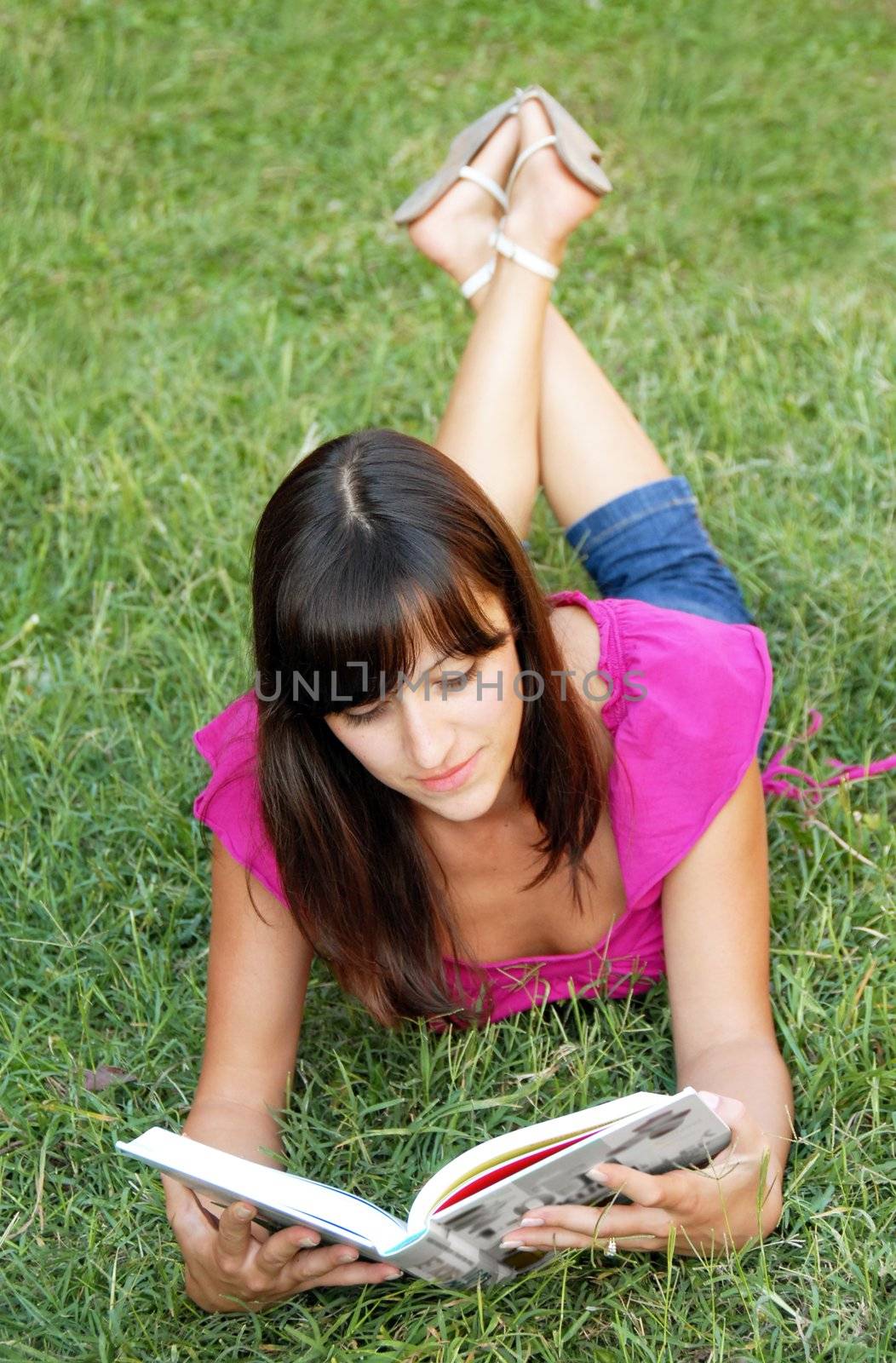 young woman lying reading a book in grass outdoor
