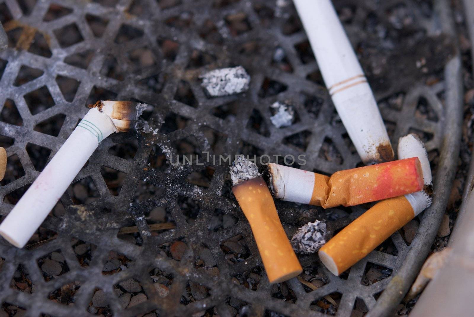 A dirty ashtray with smoked cigarette filters and butts with lipstick on them
