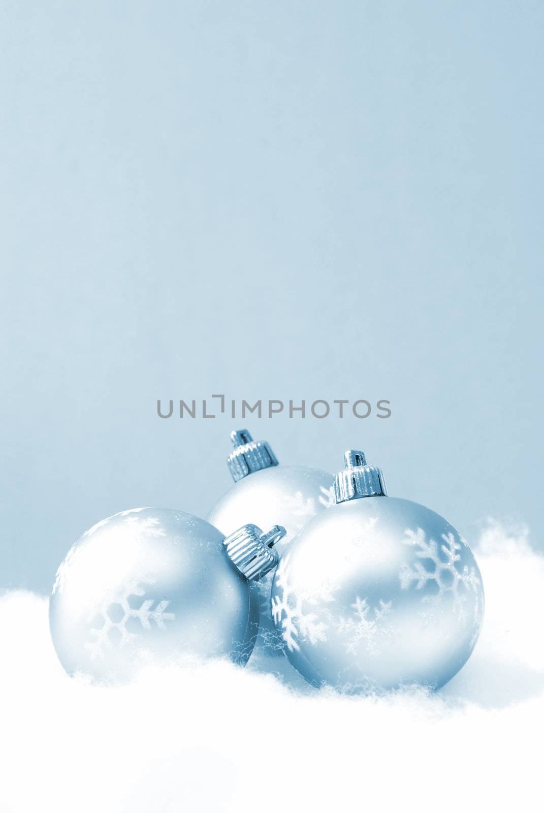 Three holiday baubles on some fake snow and coloured in blue monochrome.