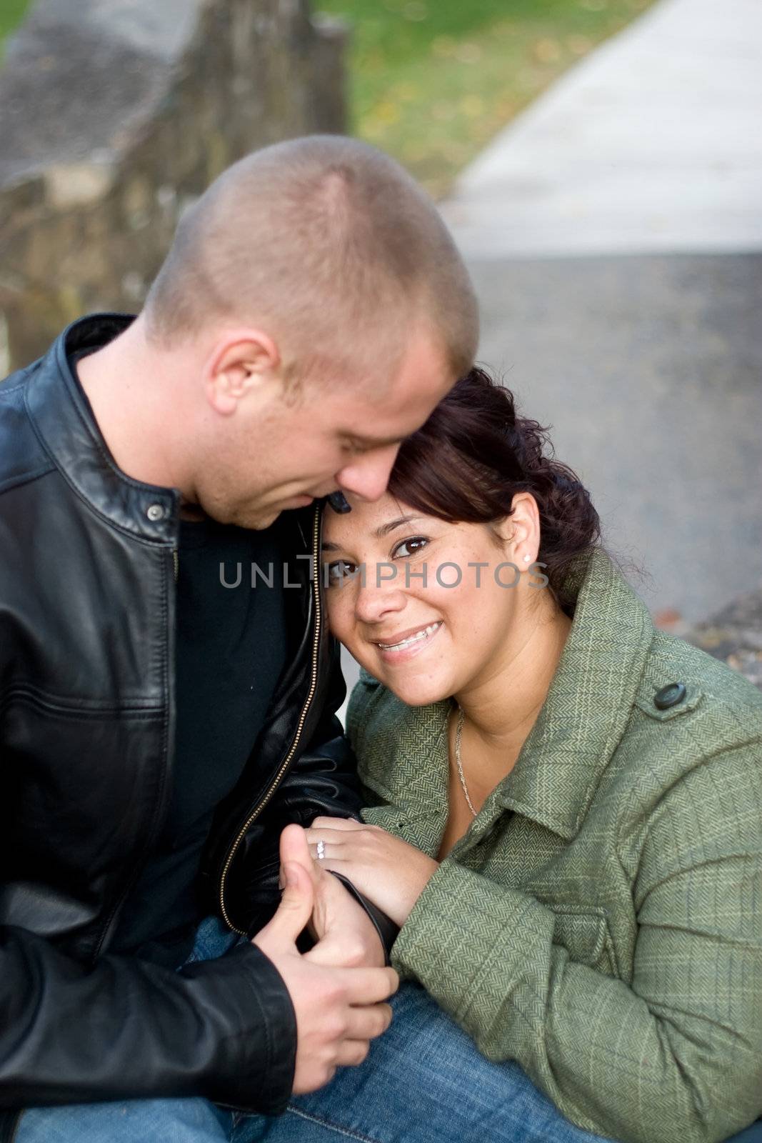 A happy interracial couple cuddling together outdoors. Shallow depth of field.