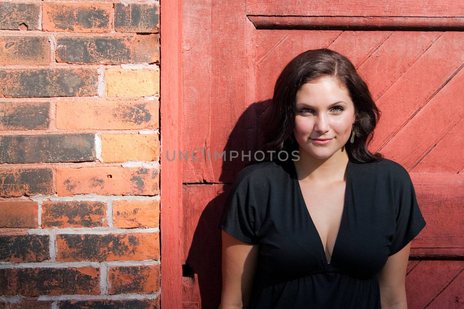 A pretty young woman in a black dress leaning against an old doorway. 