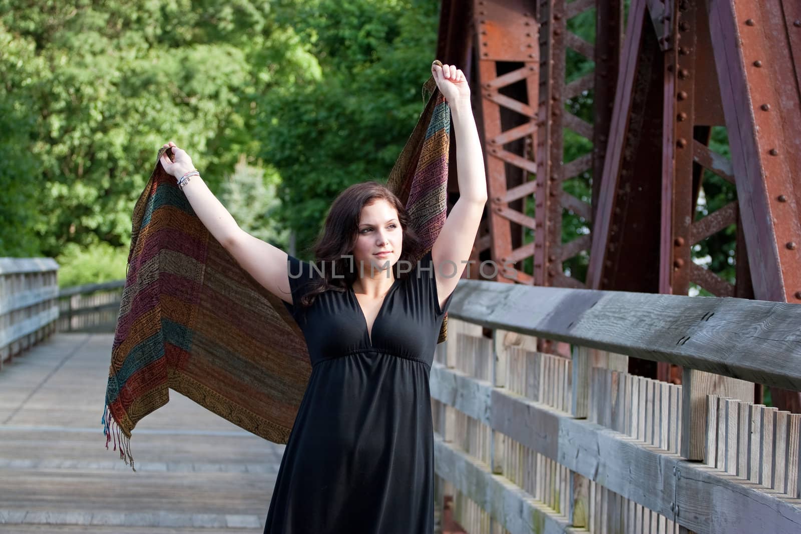 A carefree brunette woman running along a bridge with a scarf blowing in the breeze.