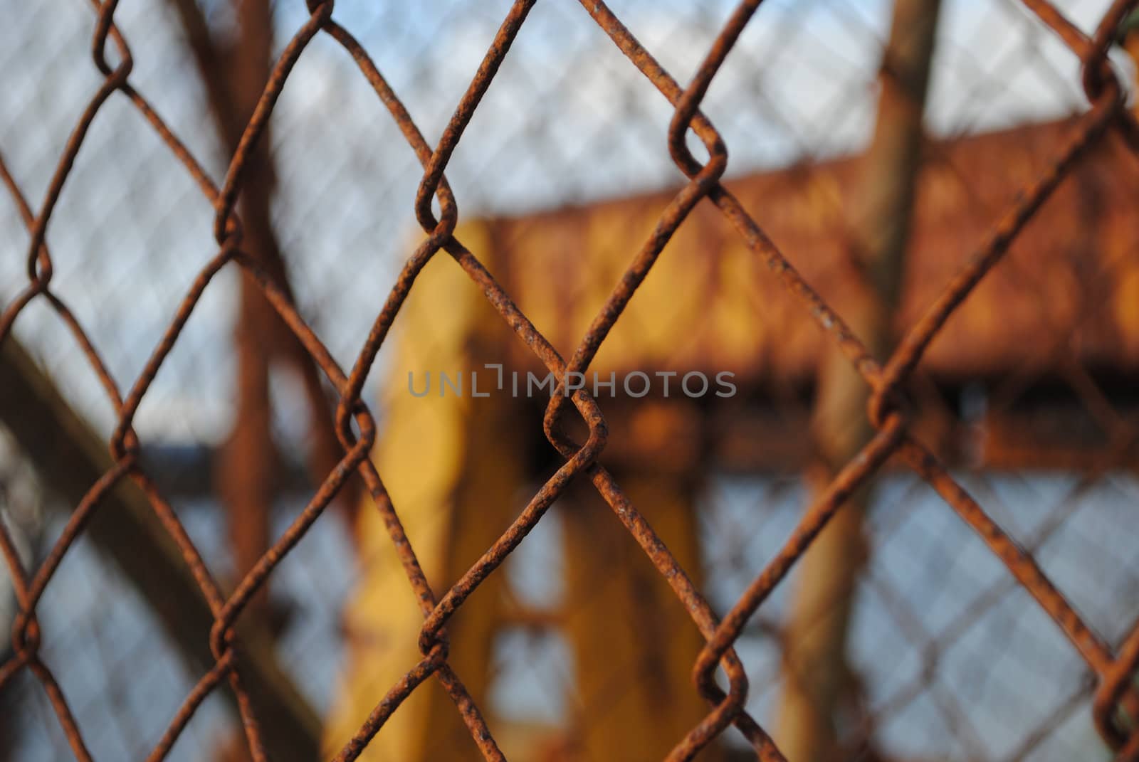 A rusty fence in front of an industrial site.