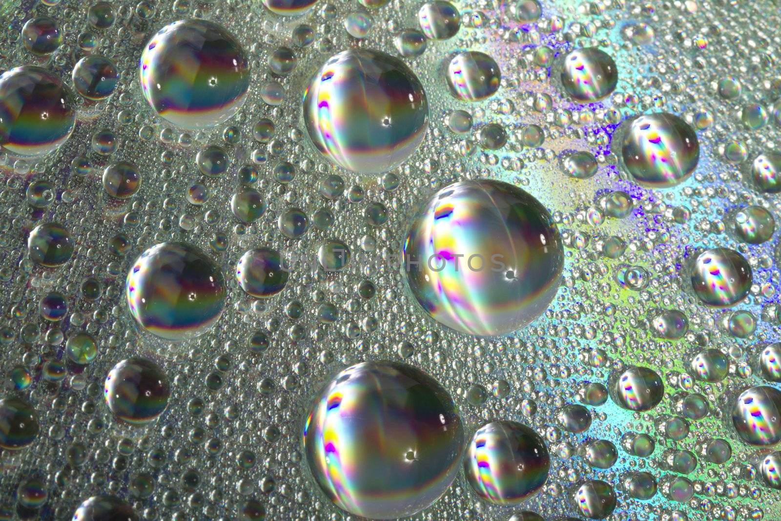 Close up view of many colorful and bright drops of water on a shiny surface.