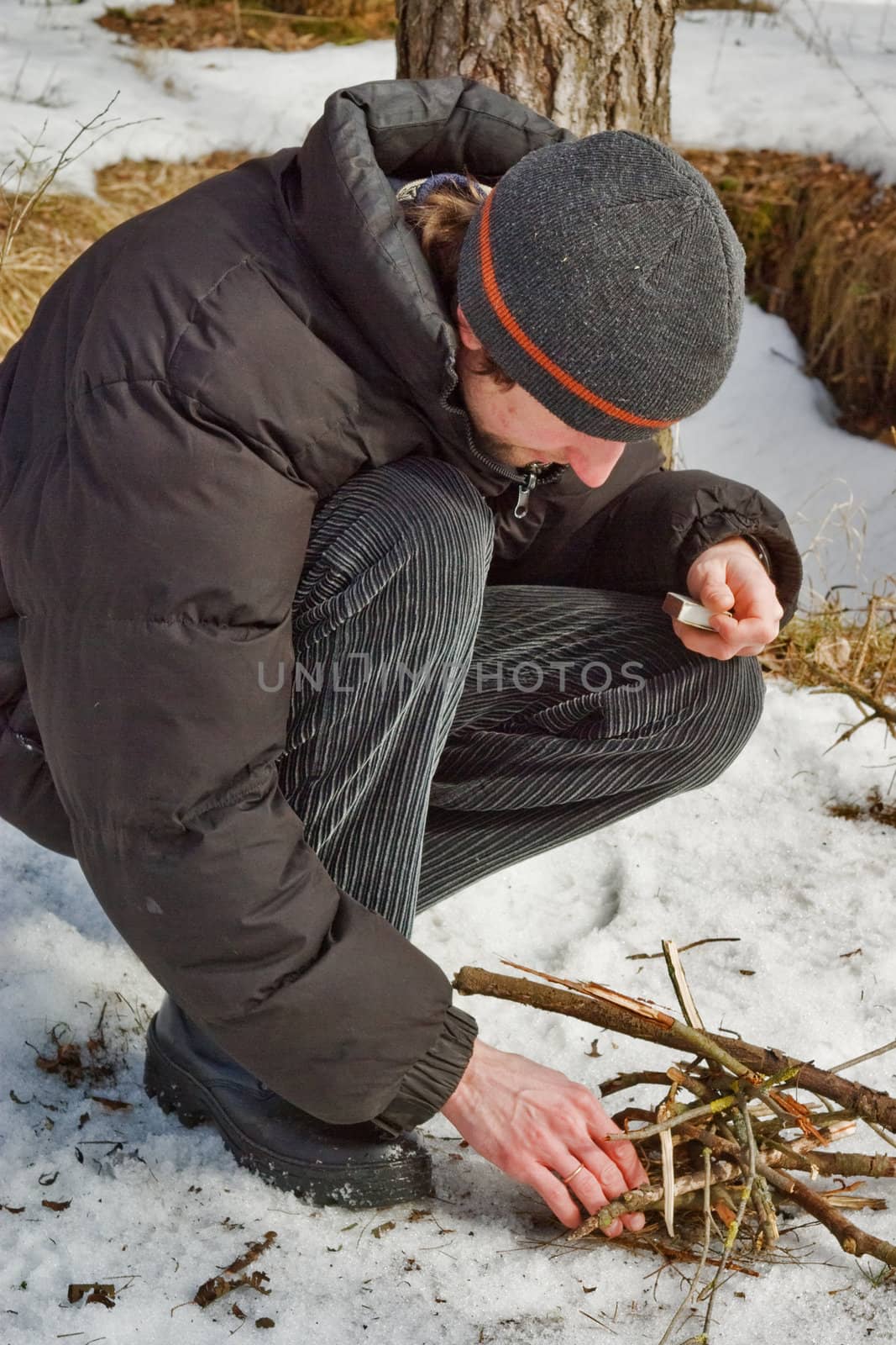 The young man kindles a fire in winter wood