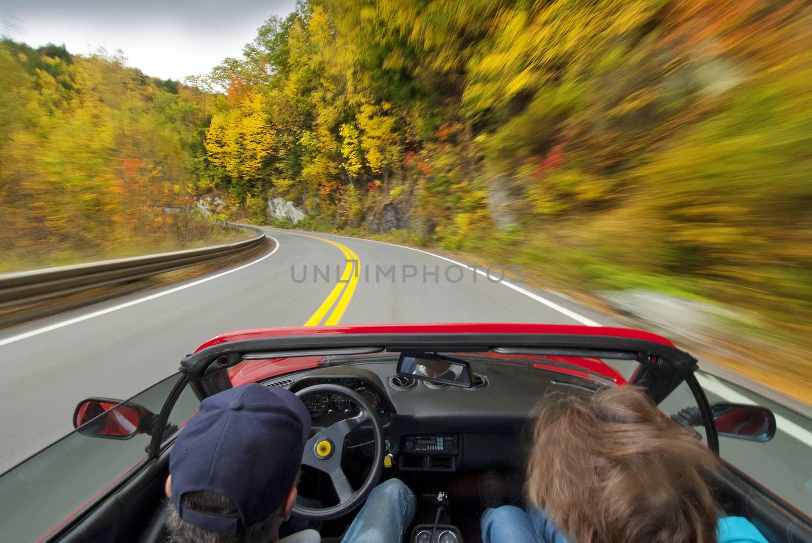 couple in a red sports car driving on winding road with fall colors
