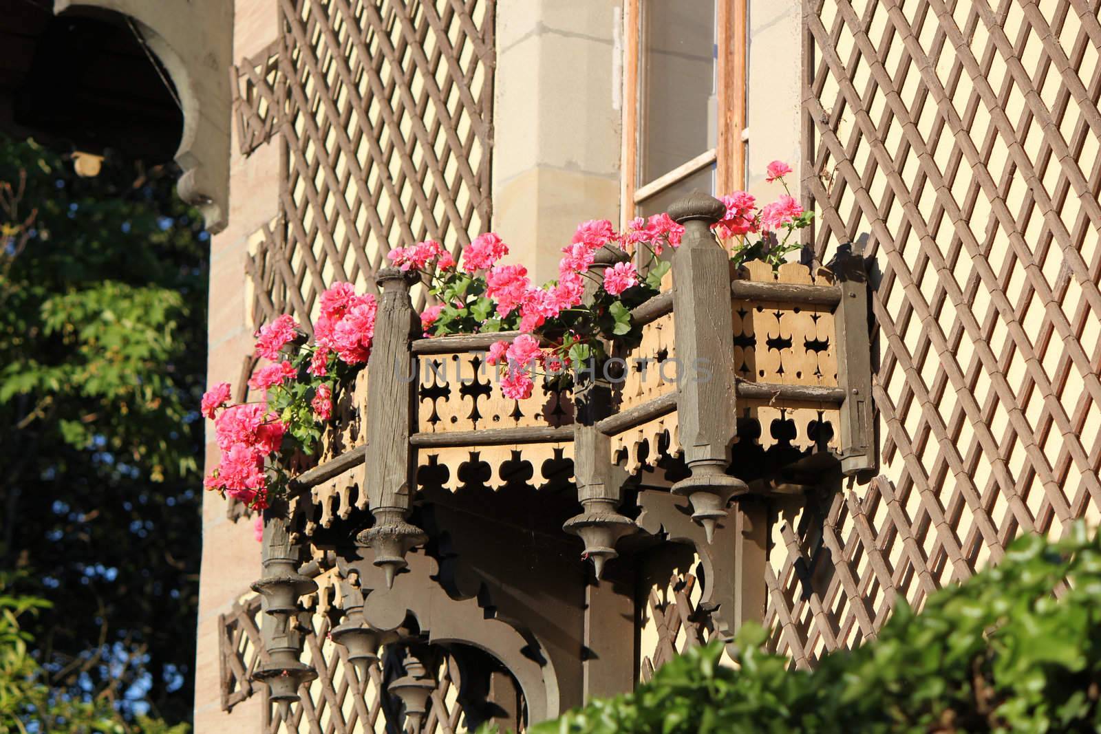 Beautiful pink flowers on a sculpted balcony made of wood in an old house