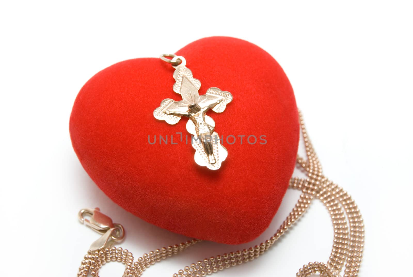 The gold cross with Jesus Christ's image lays on red velvet heart


