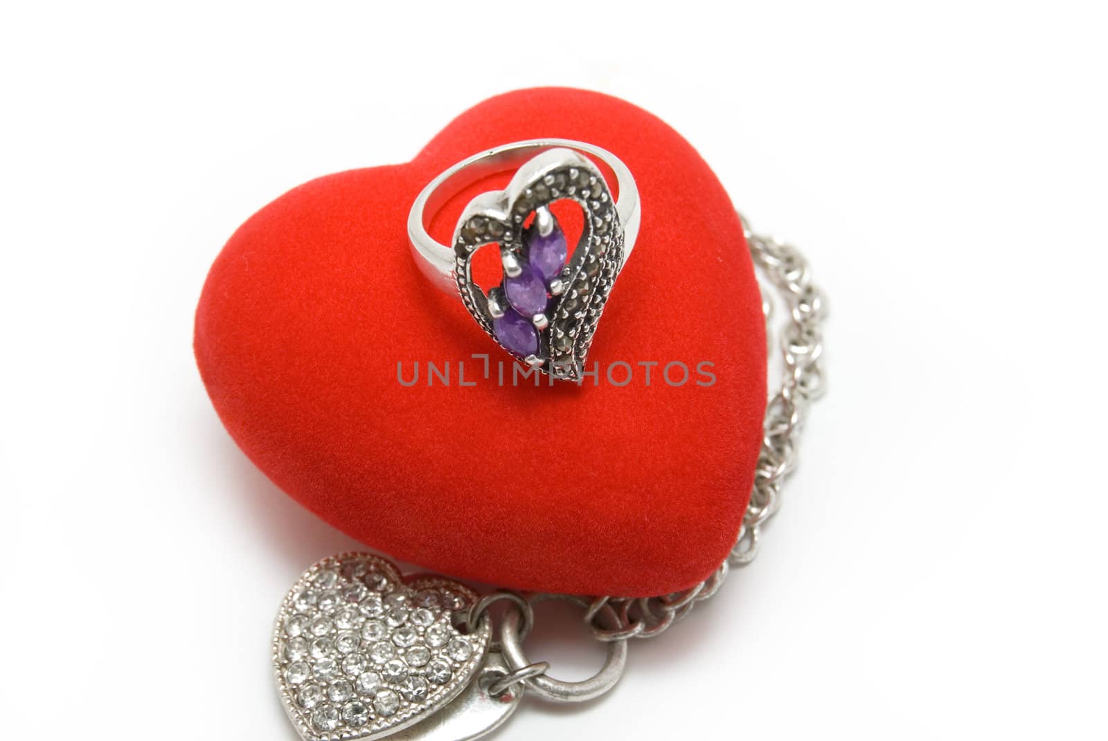 The silver ring with violet stones lays on red velvet heart
