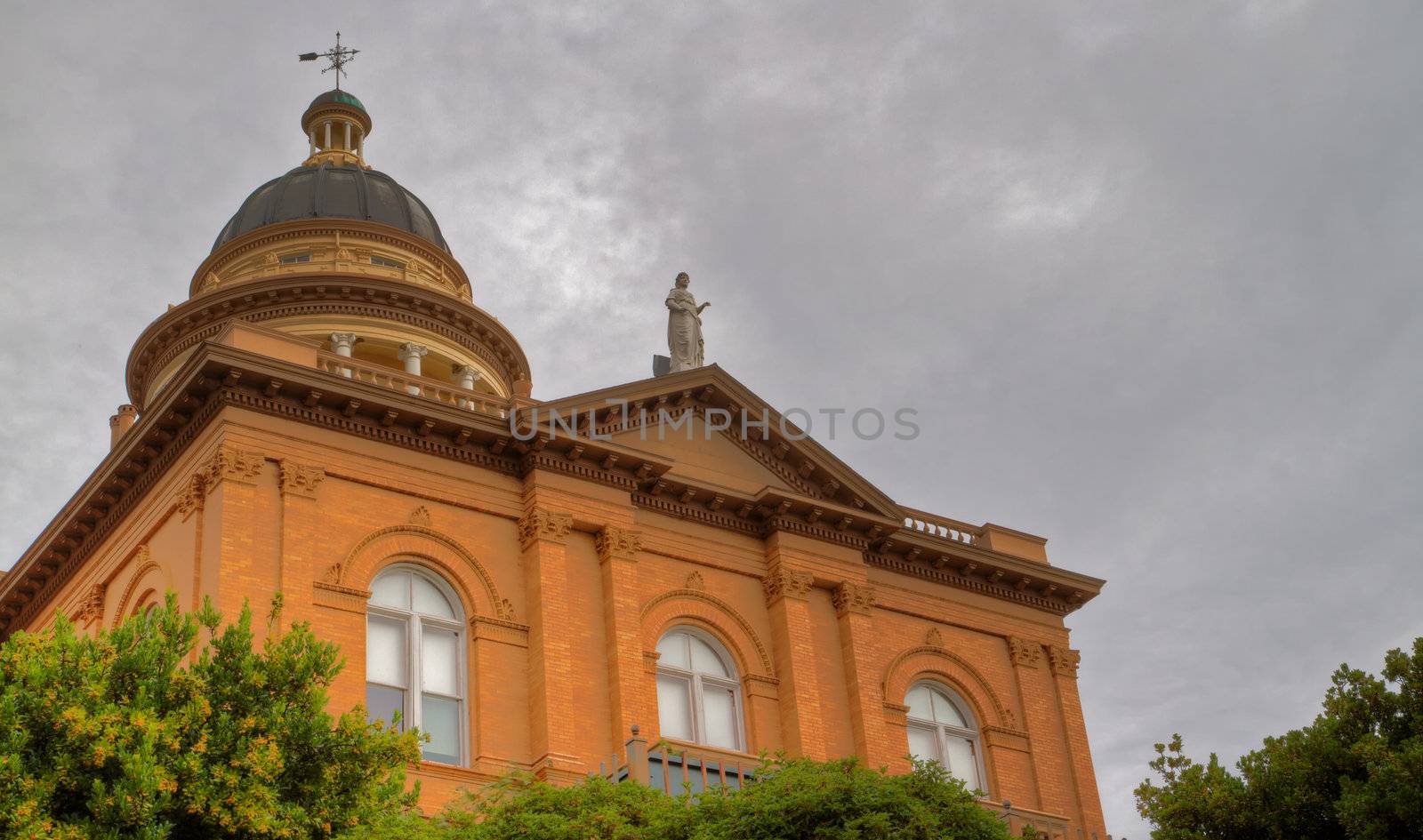 Front facade of pillared tan brick courthouse with statue on top