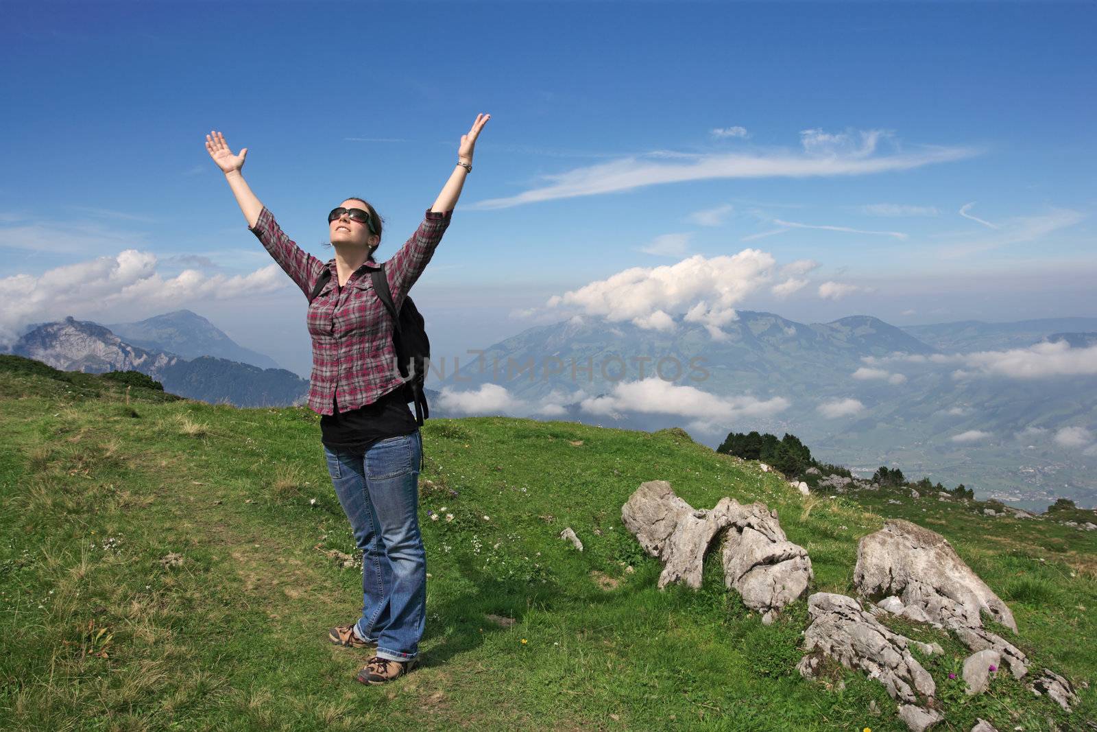 Photo of an active female with backpack and hands pointing to the sky while hiking up a mountain trail.