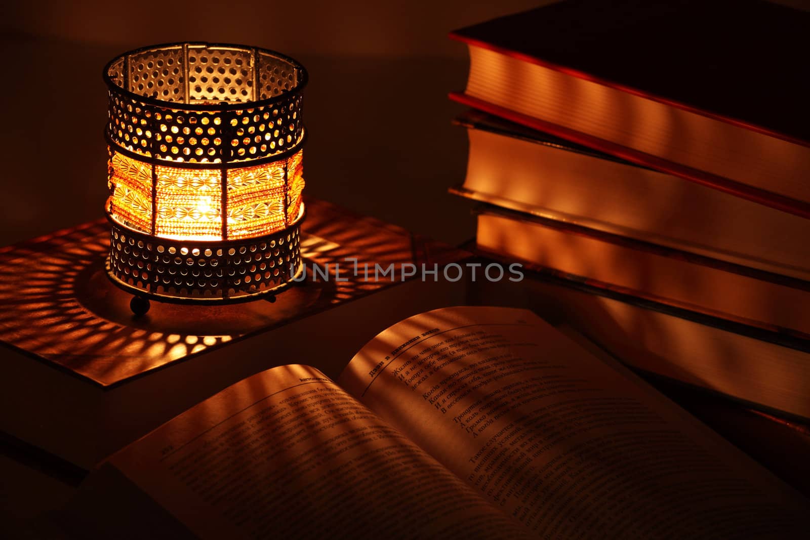 Old-style candlestick with flaming candle inside and some books in the dark