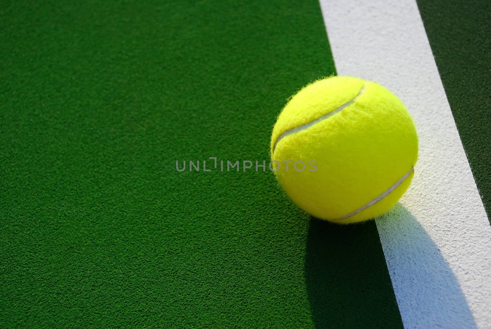 Close up of a yellow tennis ball resting on the white foul line