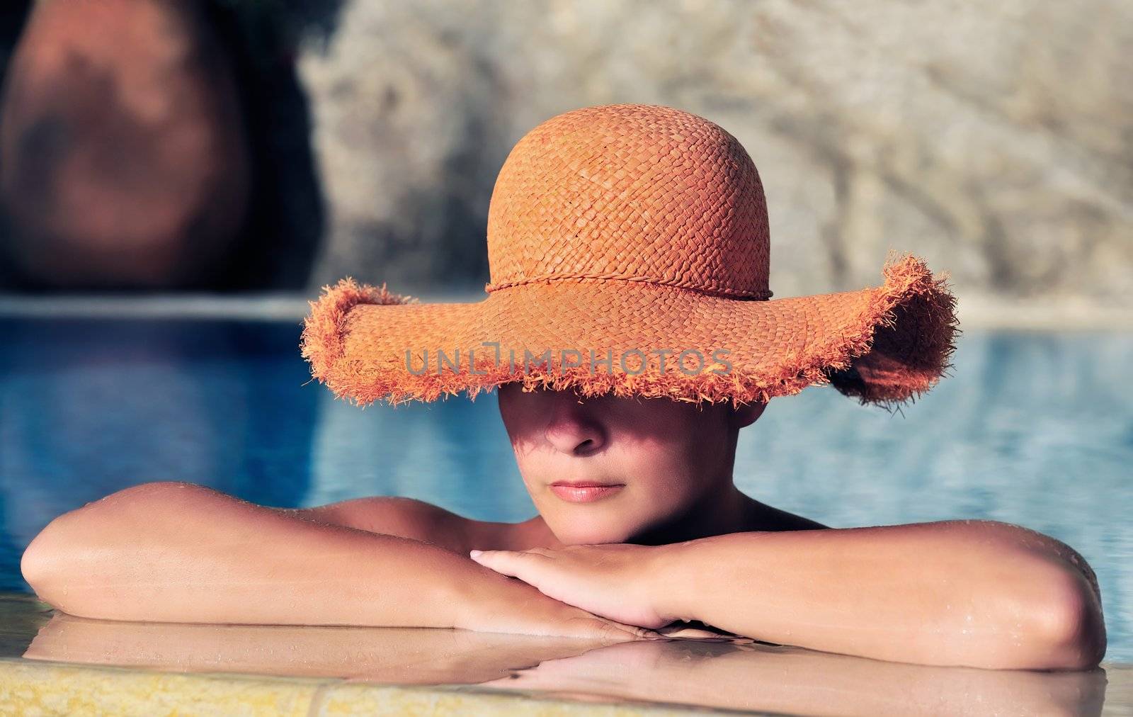 Young attractive caucasian woman in a straw hat, resting by the side of a swimming pool