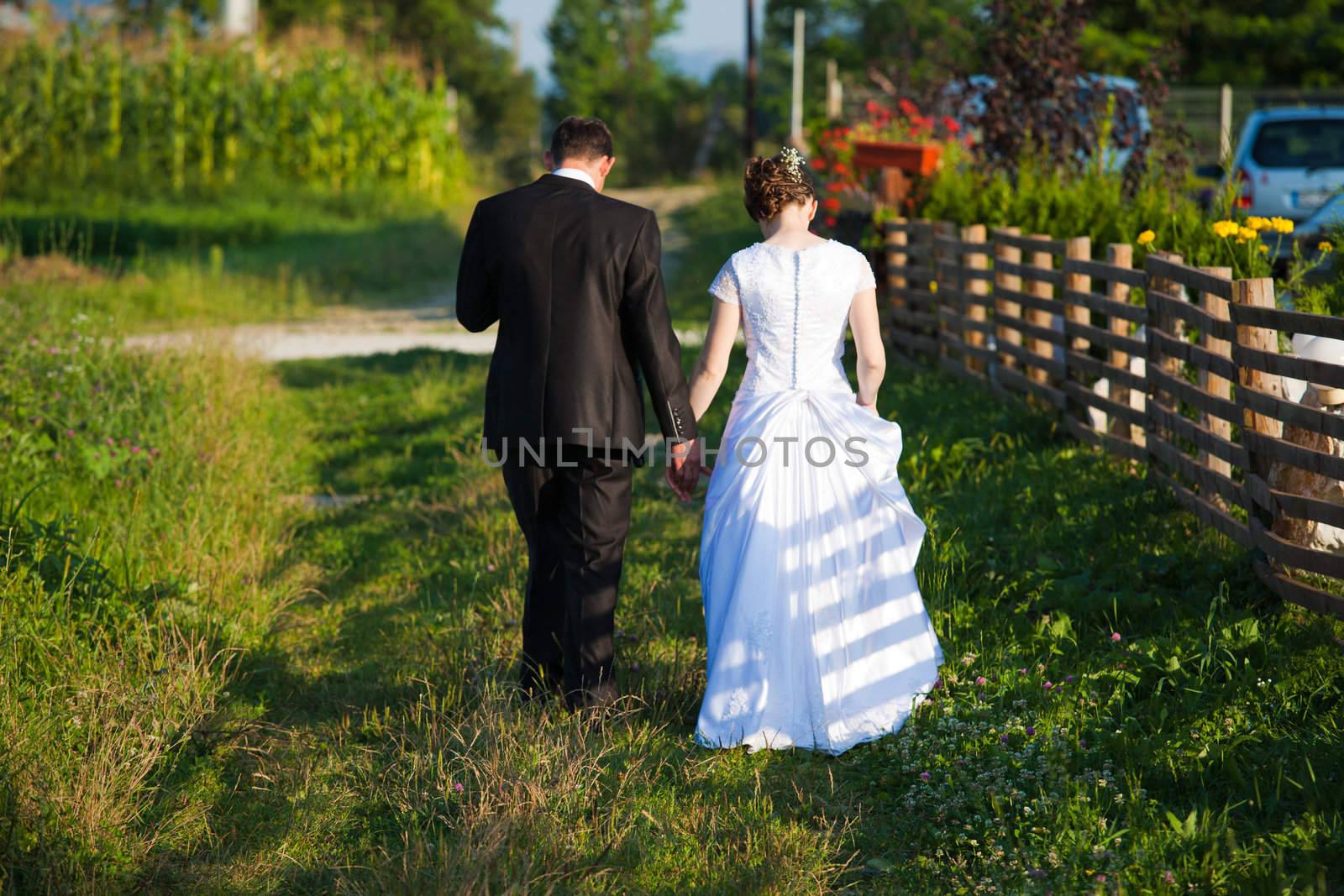 Young married couple holding hands and walking away on a countryside trail