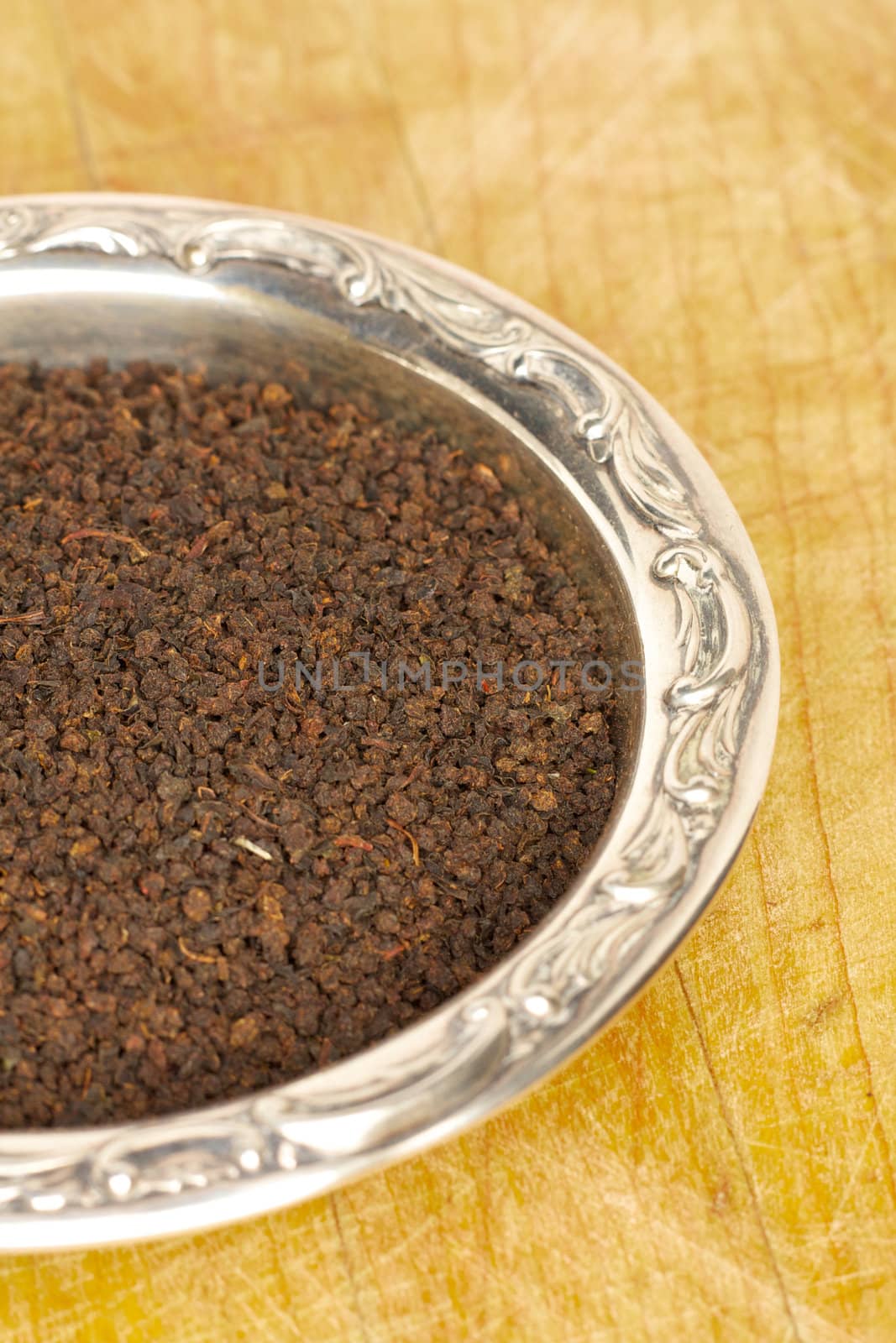 Loose black tea leaves in a sterling silver dish on a wooden surface