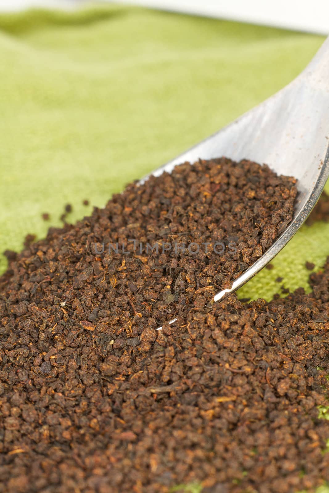 Loose black tea leaves spill from a spoon onto green linen