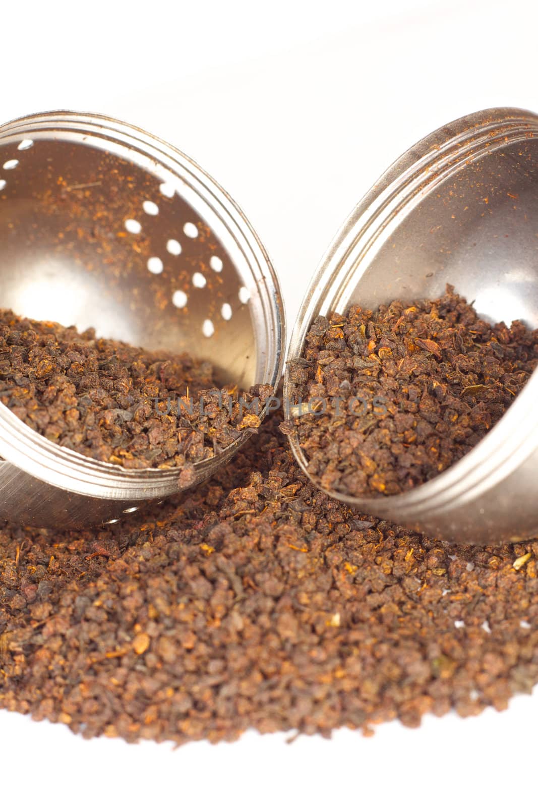 Loose black tea leaves spill from a tea strainer onto white