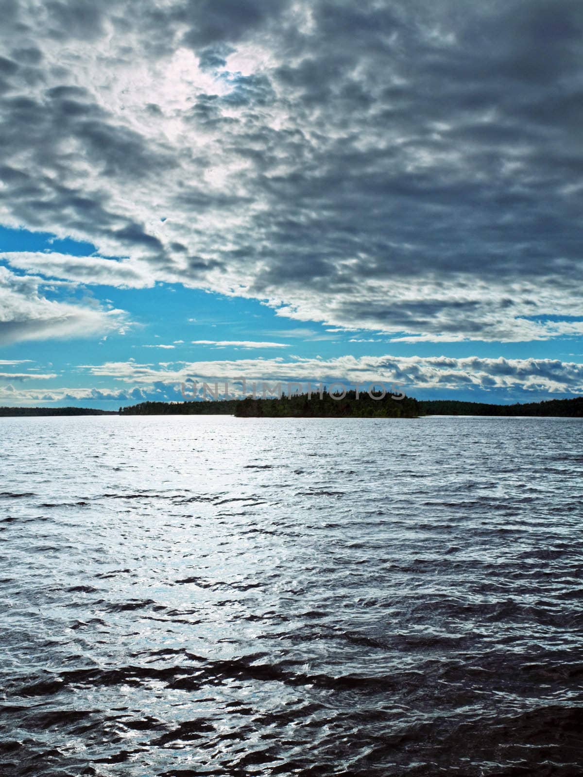 The sun through clouds shines cold waters of northern lake