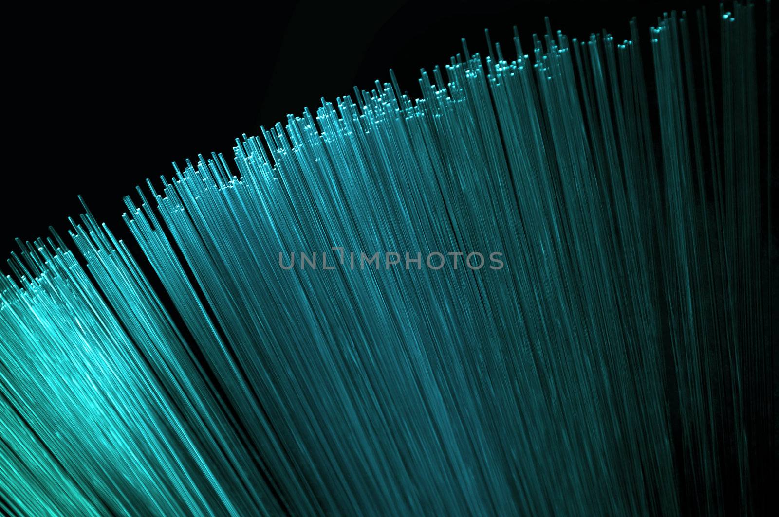 Abstract style close up on the ends of many bright cyan illuminated fiber optic light strands arranged over black.