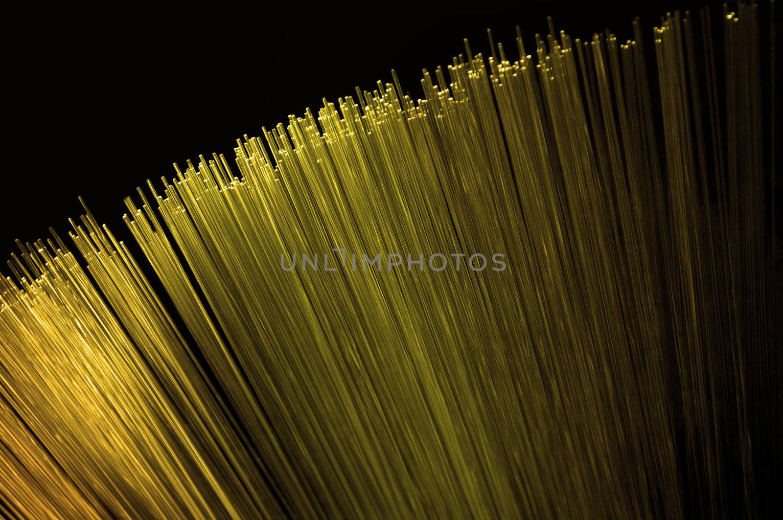 Close up on the ends of many illuminated golden fiber optic light strands arranged over black.