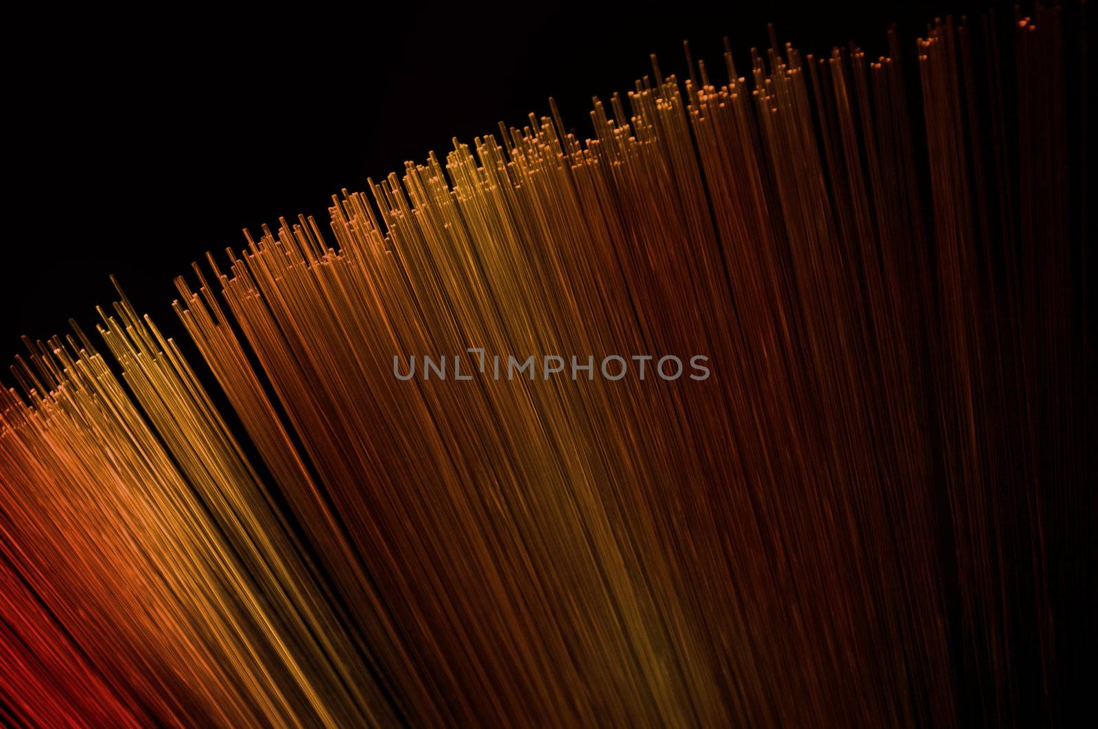 Close up on many illuminated gold, red and orange fiber optic light strands arranged over black