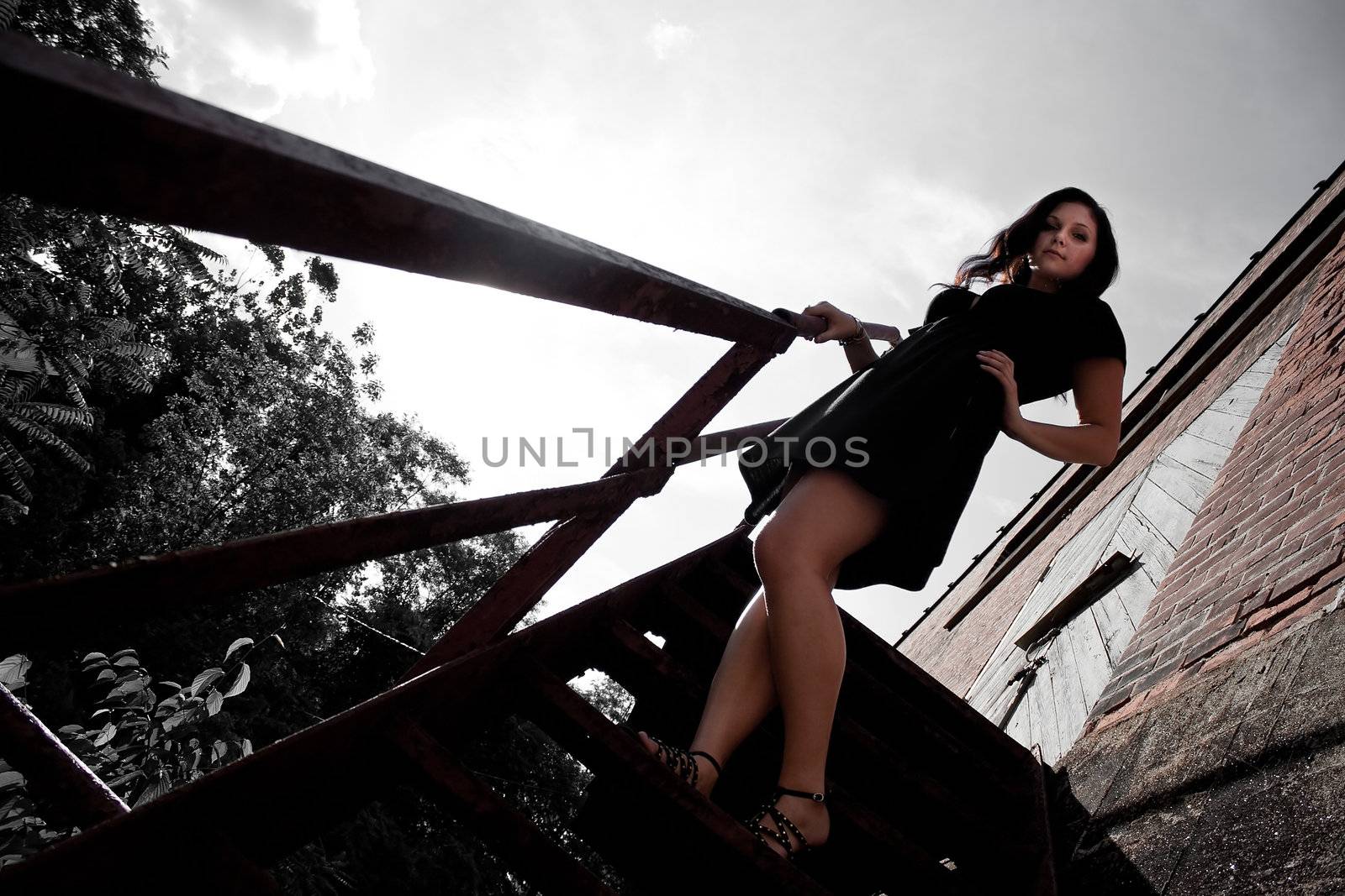 A young lady poses on a rusted old stairway in an urban setting.  Selective color.