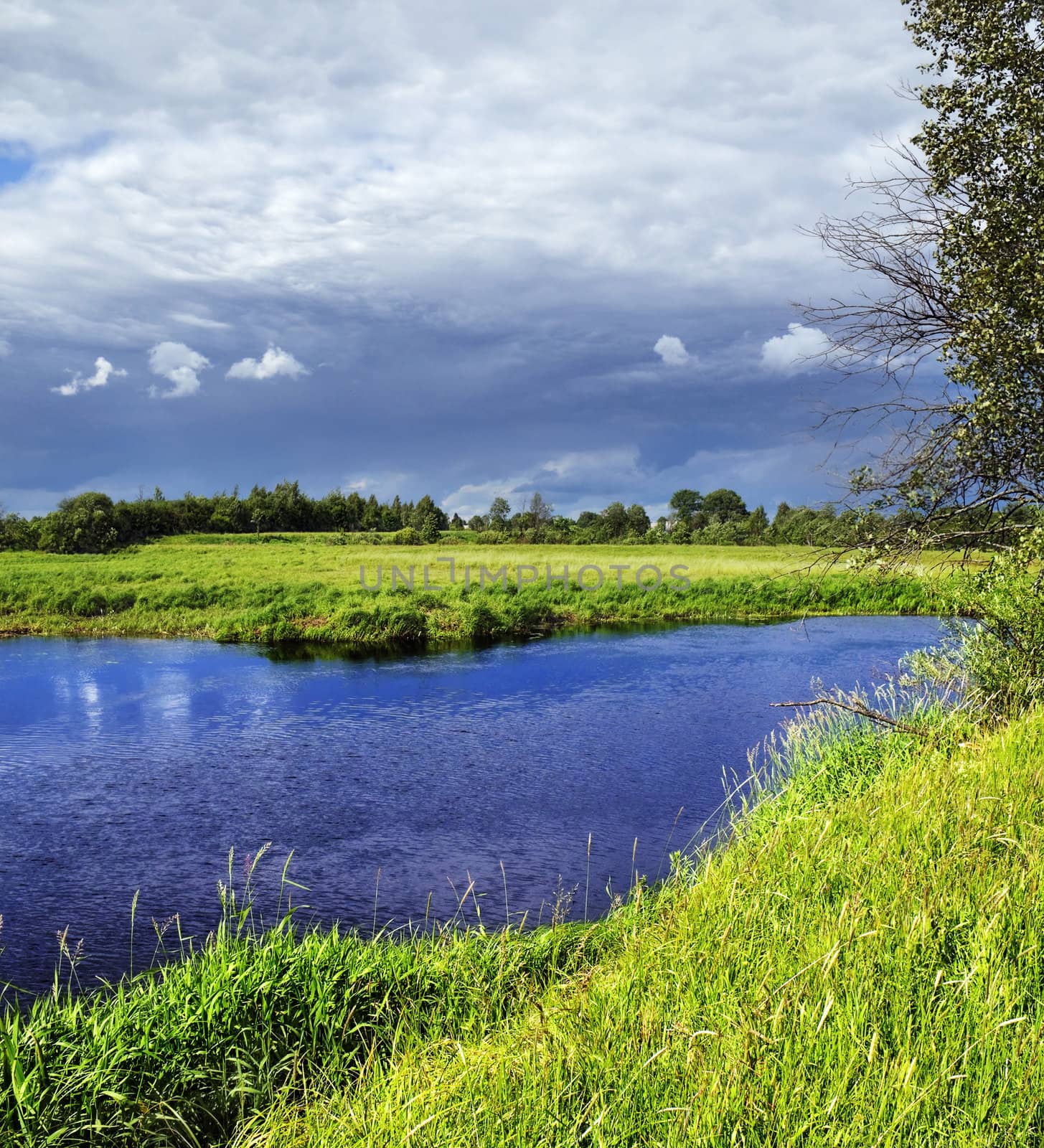 Dark clouds over the dark river and a green grass