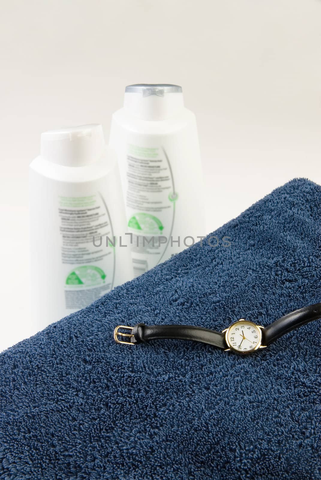 Bath time concept with two towels, a watch, and some shampoo and coditioner, isolated against a white background.