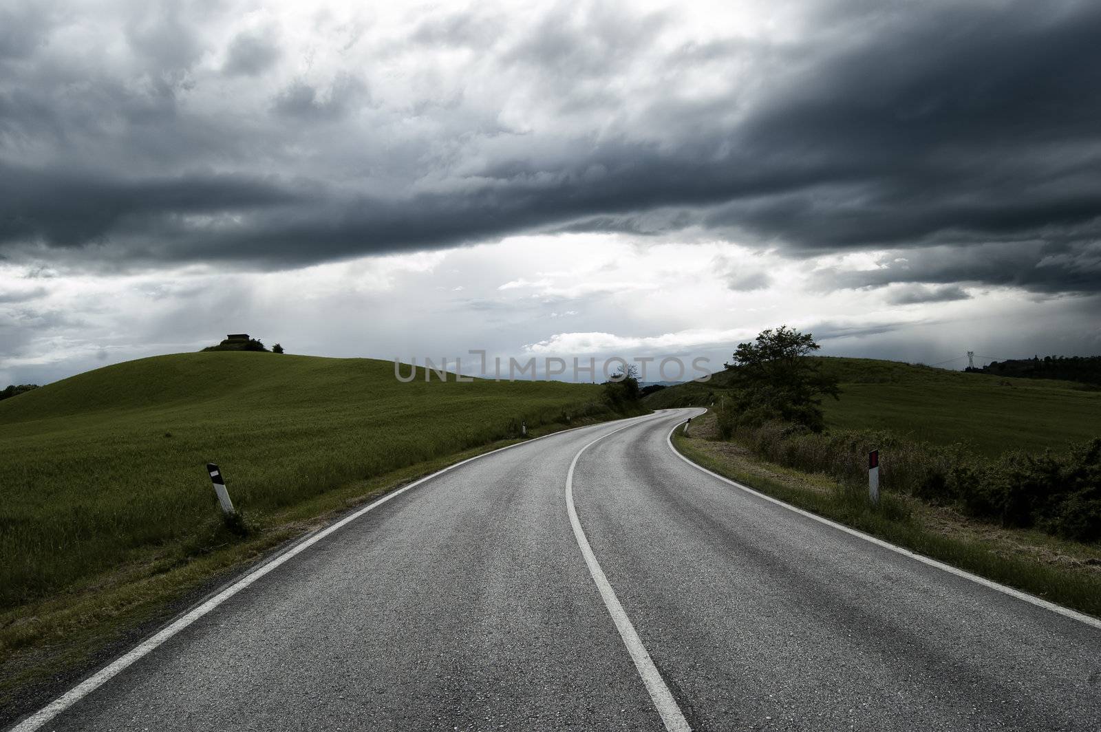 Road between fields under a cloudly sky