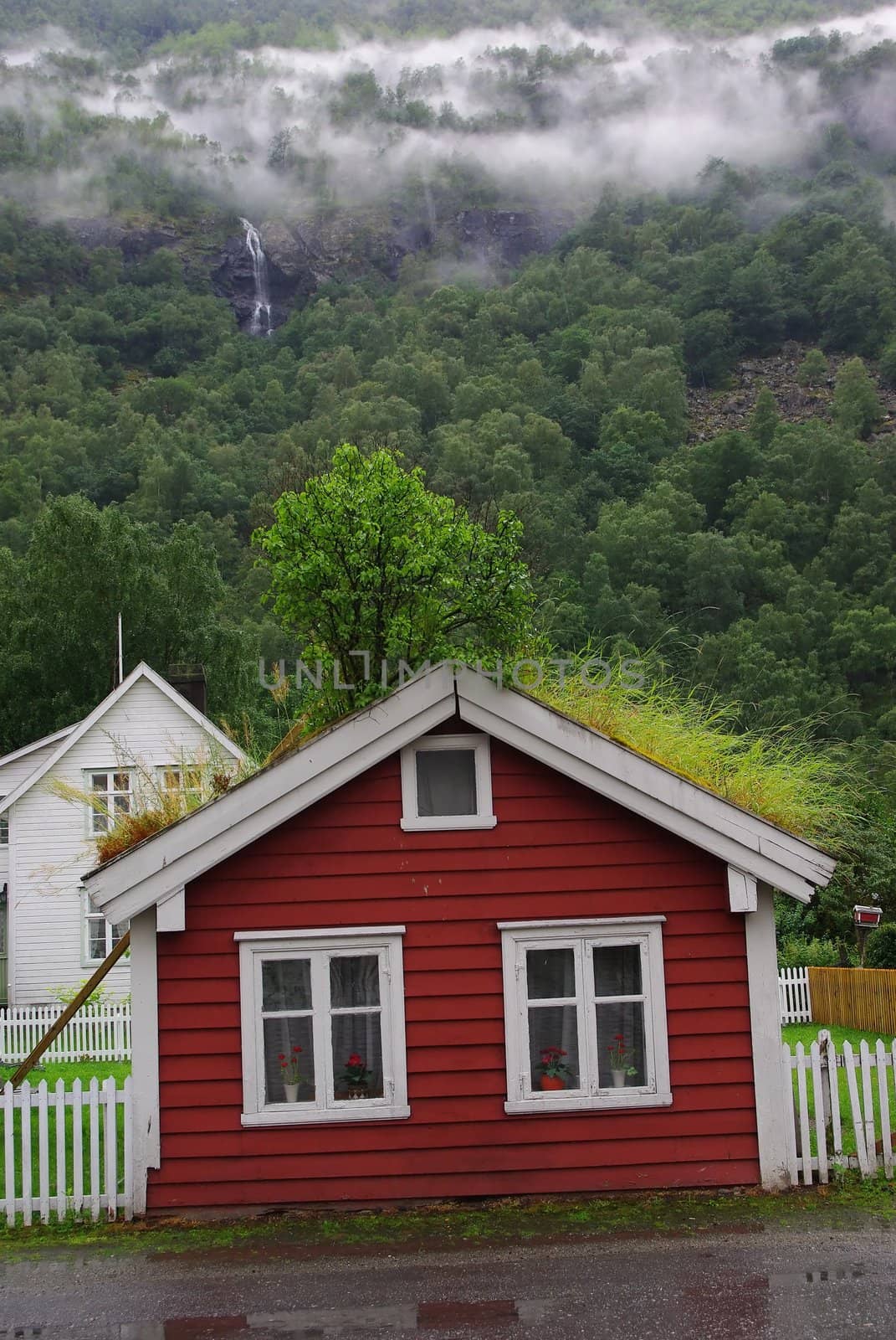 Little red house with  roof of grass on green hillside  background with clouds and mountain river