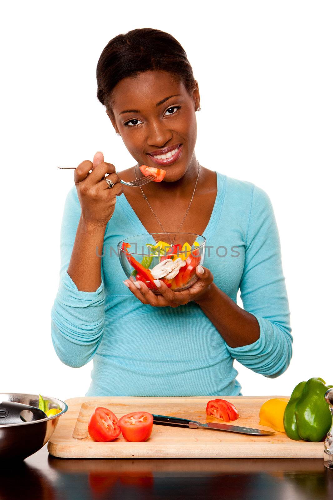 Beautiful attractive happy smiling health conscious vegetarian  young woman eating healthy fresh organic salad from a bowl, standing at kitchen counter with chopping board, isolated.