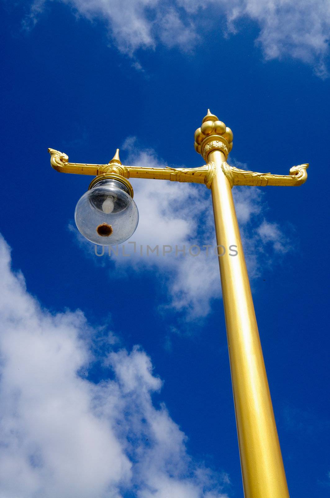 a gold-colored lamp post standing in the blue sky by ekawatchaow