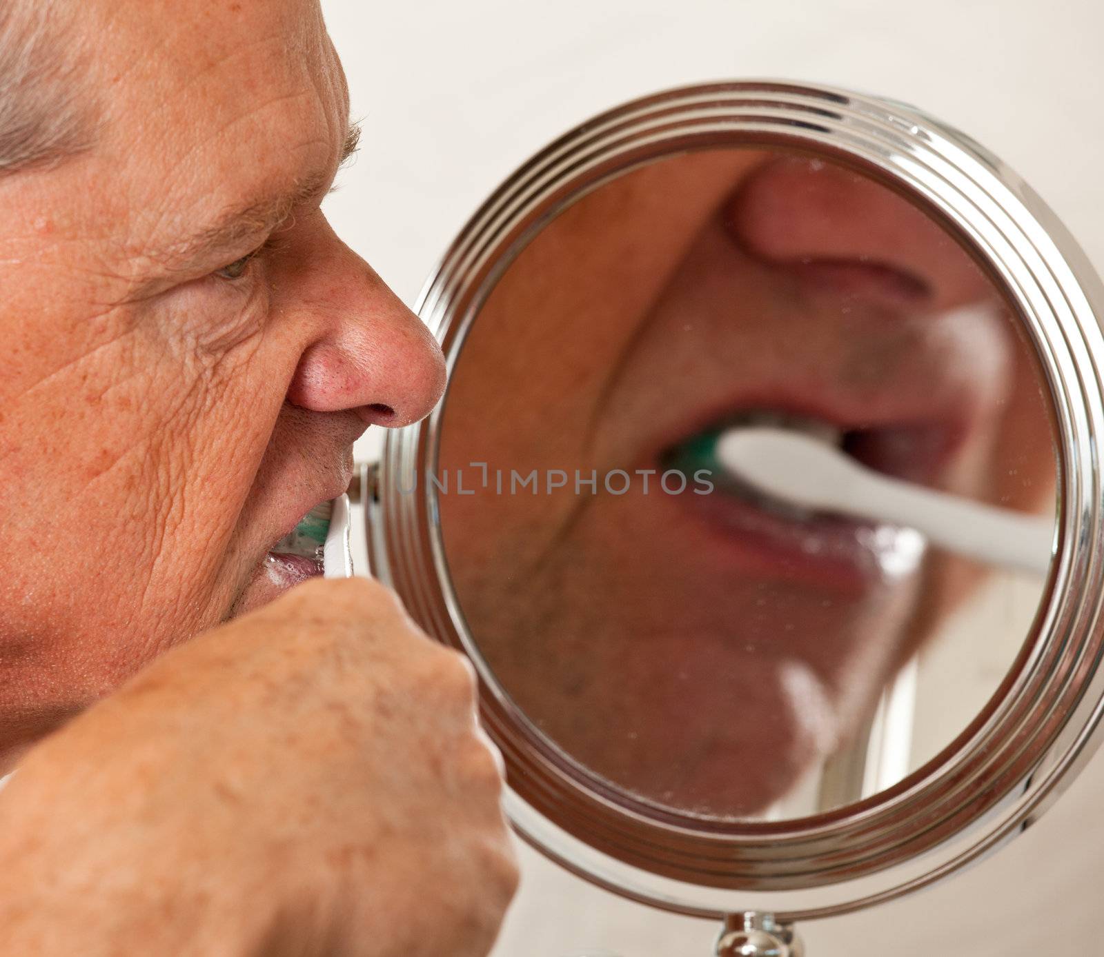 Middle aged man cleaning teeth in front of shaving mirror with electric toothbrush