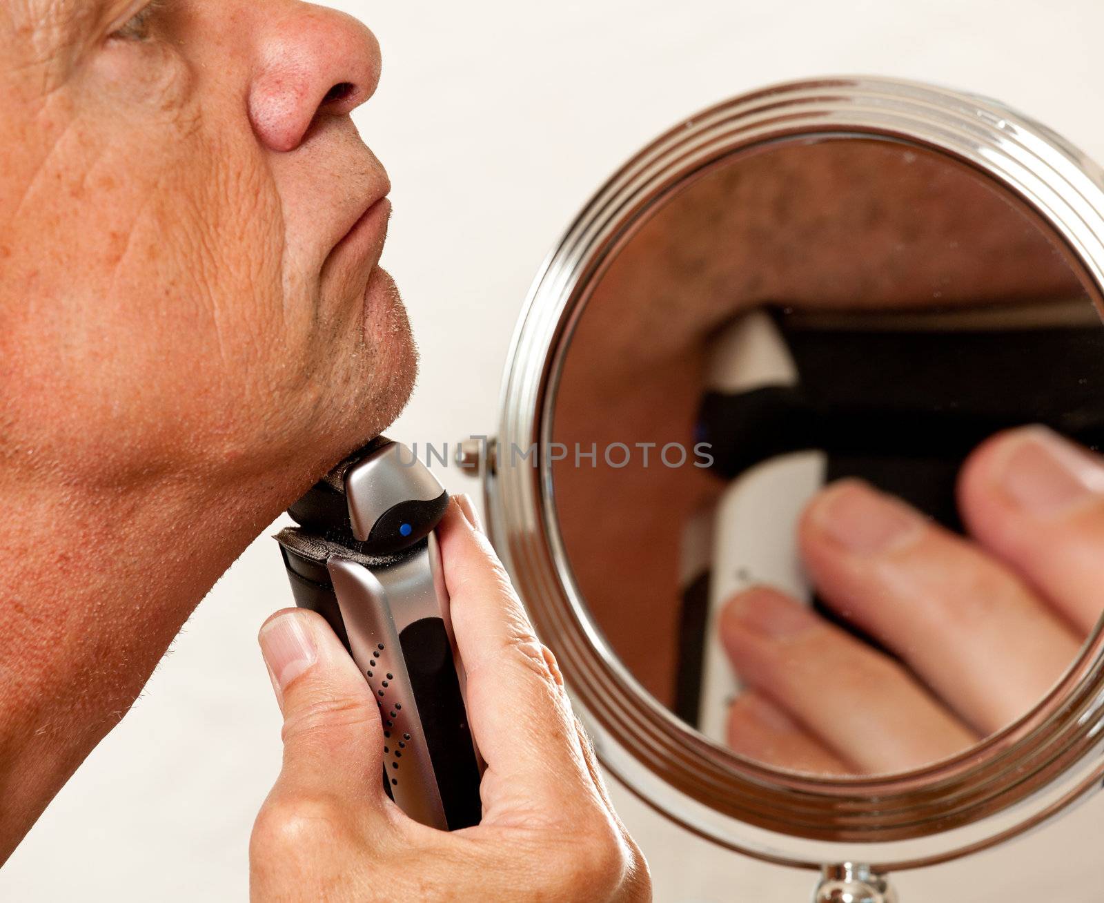 Retired male shaving with electic razor in front of magnifying mirror