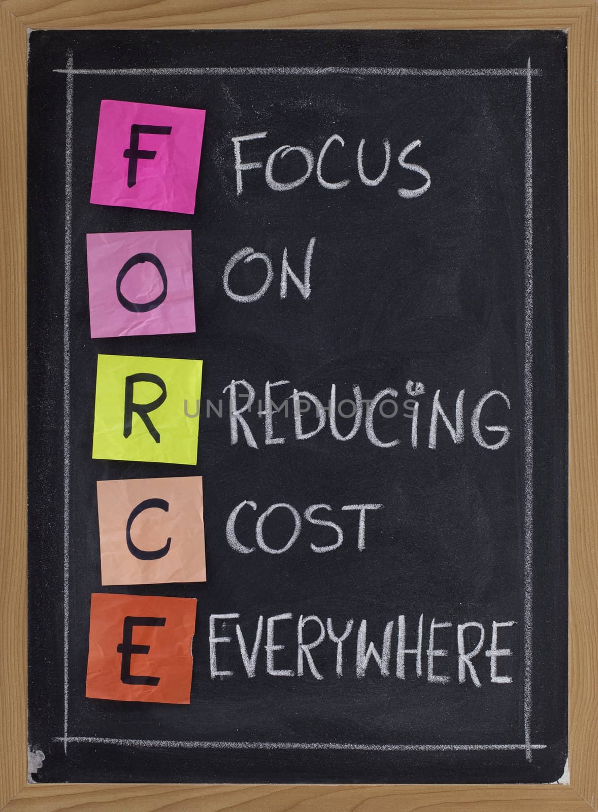 FORCE acronym (focus on reducing cost everywhere) - white chalk handwriting and color sticky notes on blackboard
